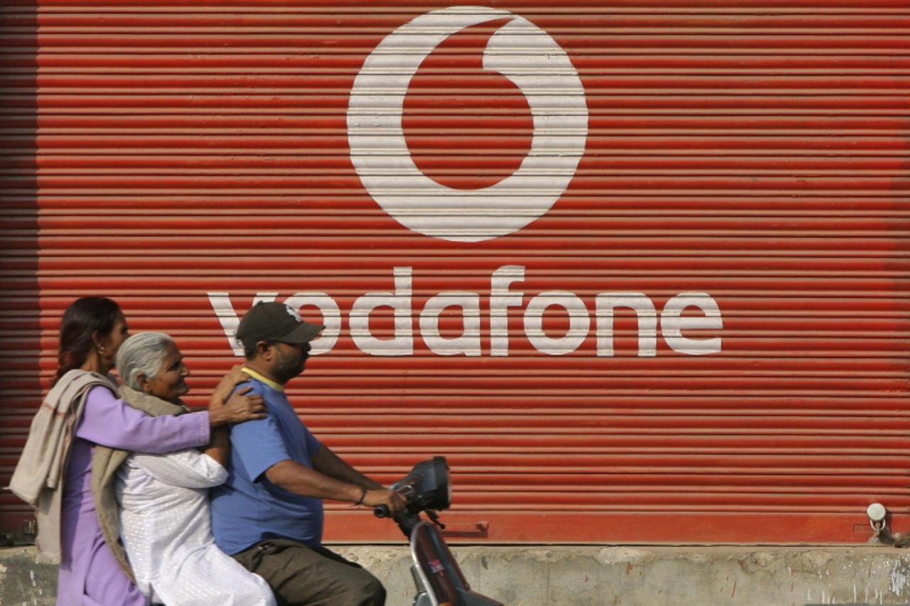 \'A man and two passengers ride on a scooter past a shop displaying the Vodafone logo on its shutter in Jammu November 21, 2011. India\'s federal police on November 19 conducted searches at Vodafone\'