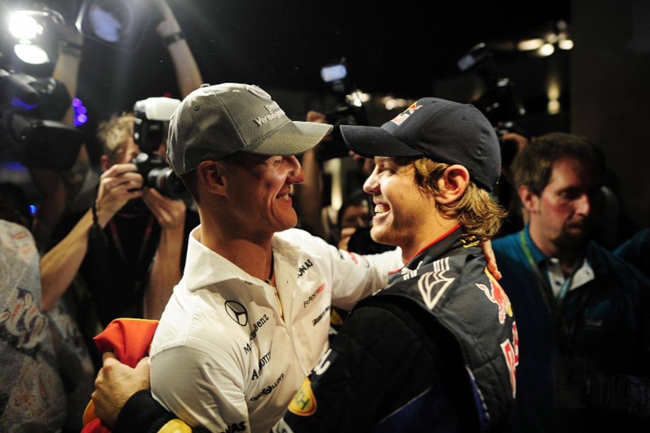 \'Red Bull\'s German driver Sebastian Vettel (R) is congratulated by Mercedes GP\'s German driver Michael Schumacher with his team members at the Yas Marina circuit on November 14, 2010 in Abu Dhabi, 