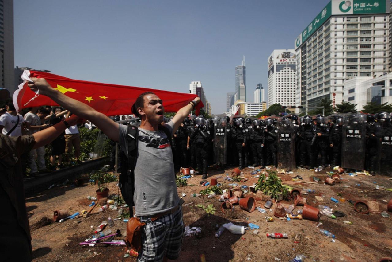 'A demonstrator shouts with a Chinese flag as he stands in front of riot police during a protest against Japan's decision to purchase disputed islands, which Japan calls the Senkaku and China calls t