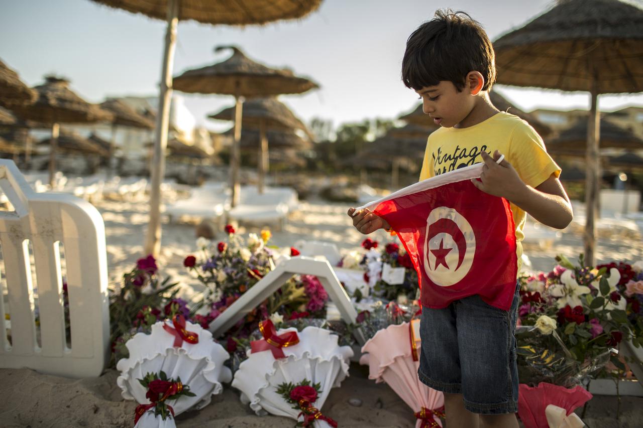 A boy holds a Tunisian flag as he stands near bouquets of flowers laid at the beachside of the Imperiale Marhabada hotel, which was attacked by a gunman in Sousse, Tunisia, June 27, 2015. Tour companies were evacuating thousands of foreign holidaymakers f