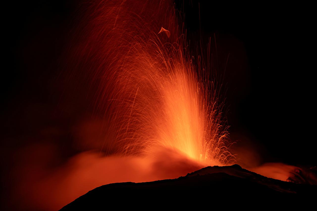 Mount Etna spurts red-hot lava into the night sky, as seen from Rocca Della Valle