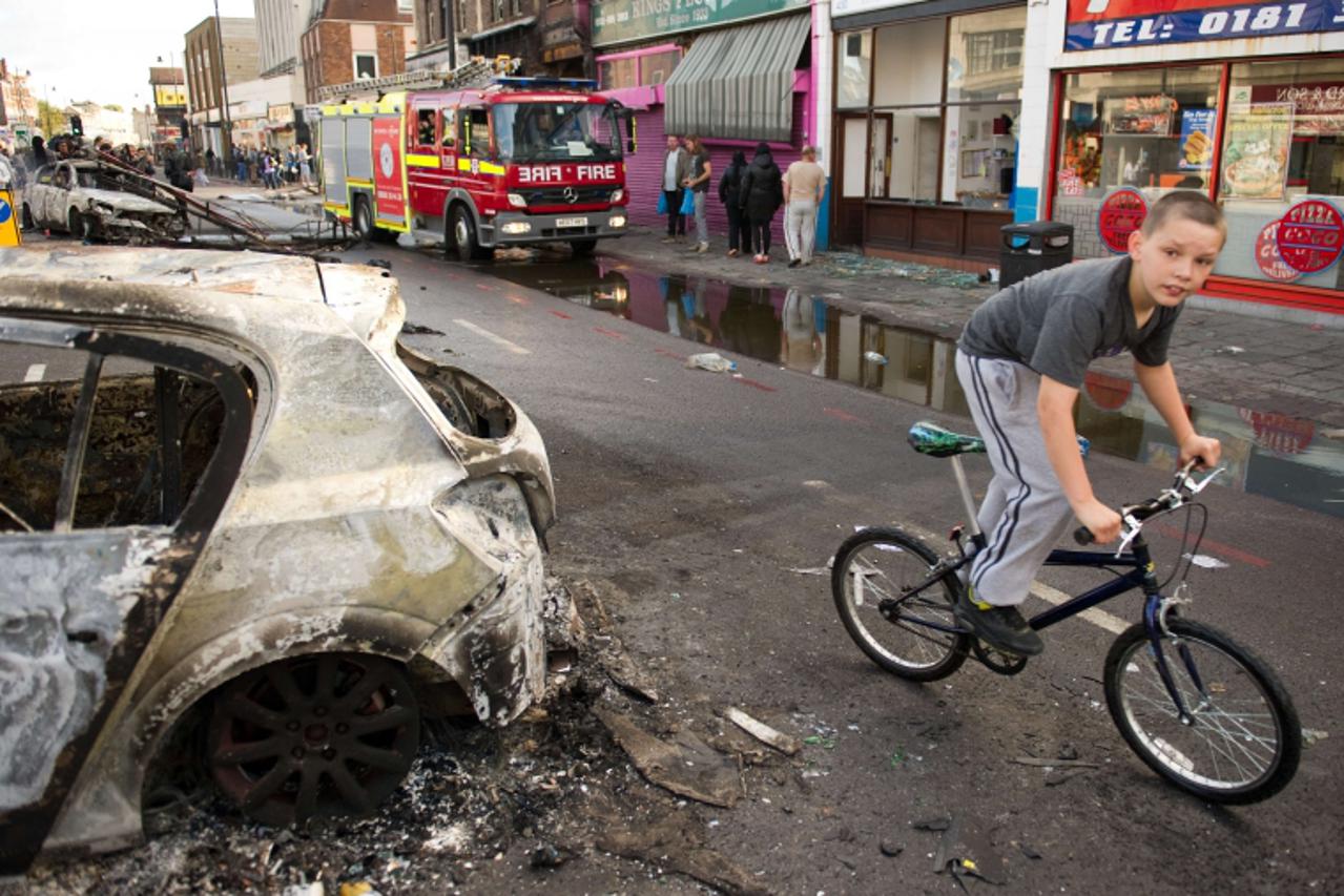 'A boy cycles past a burnt-out police car on High Road in Tottenham, north London on August 7, 2011. Two police cars and a large number of buildings were on Saturday set ablaze in north London followi