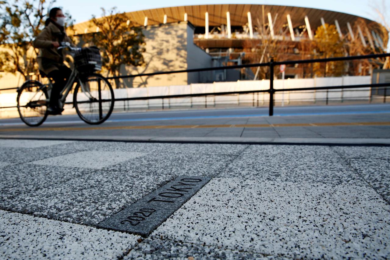 FILE PHOTO: A woman cycles past a sign for Tokyo 2020 Olympic Games on the pavement in front of the National Stadium, the main stadium of Tokyo 2020 Olympics and Paralympics, in Tokyo