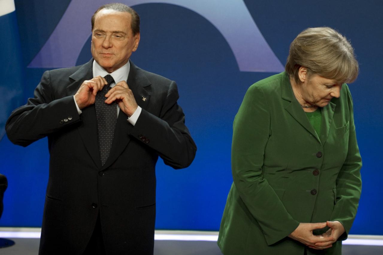 'Italian Prime Minister Silvio Berlusconi (L) adjusts his tie next to German Chancellor Angela Merkel before posing for a family photo on November 3, 2011 during the G20 Summit of Heads of State and G