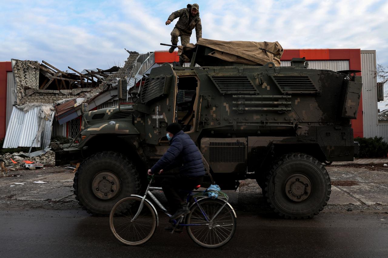 A man wearing a protective face mask rides a bike, as Russia's attack on Ukraine continues, past a soldier on an American MaxxPro military vehicle in the formerly Russian occupied city of Lyman, Donetsk region of Ukraine