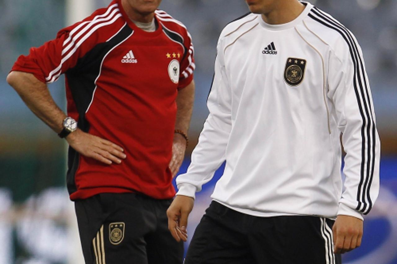 'Germany\'s Lukas Podolski (R) walks past coach Joachim Loew during a training session in Cape Town July 2, 2010. REUTERS/Ina Fassbender (SOUTH AFRICA - Tags: SPORT SOCCER WORLD CUP)'
