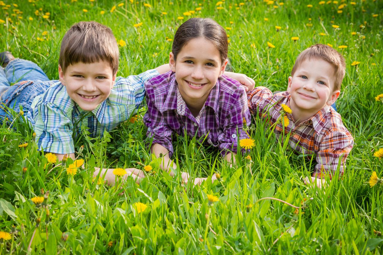 Three smiling kids lying together on green grass meadow