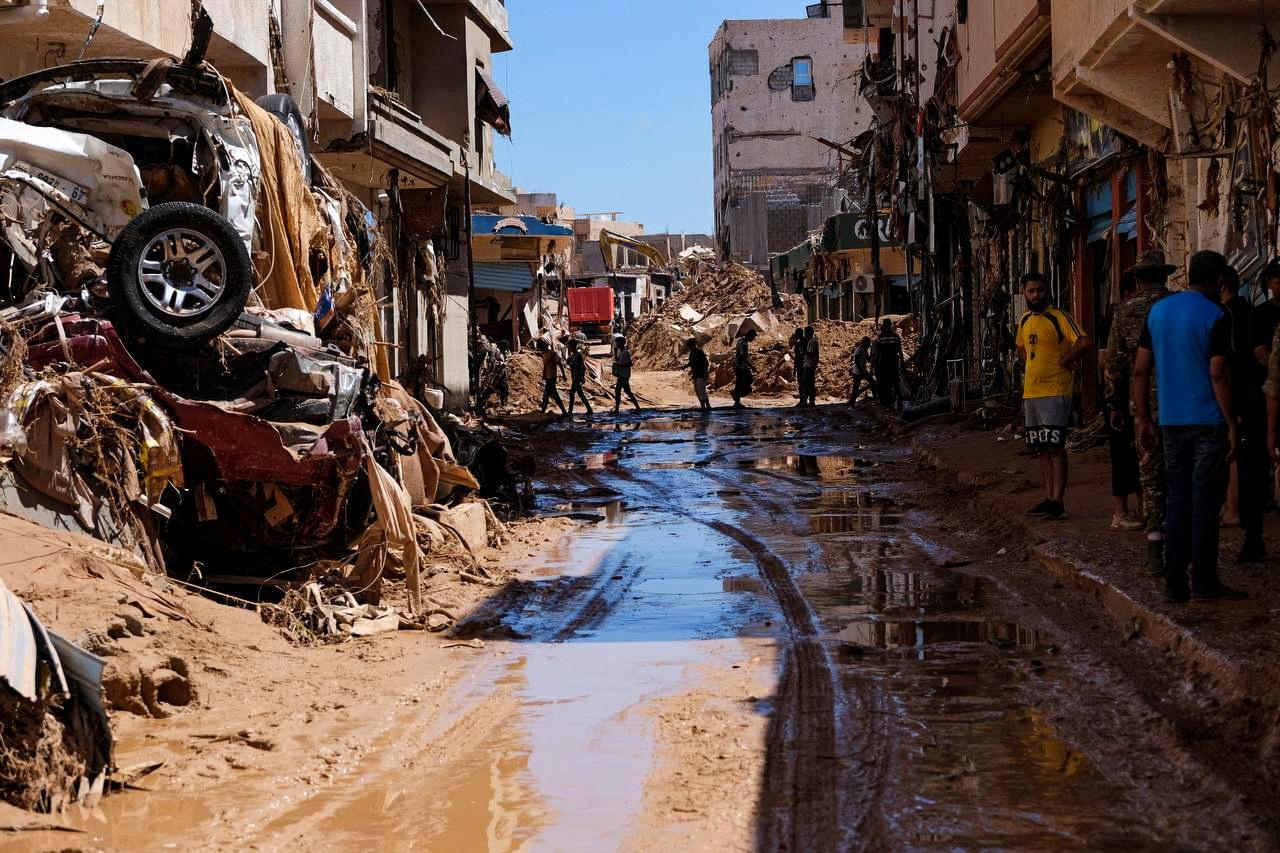 People walk next to damaged houses, following a powerful storm and heavy rainfall hitting the country, in Derna