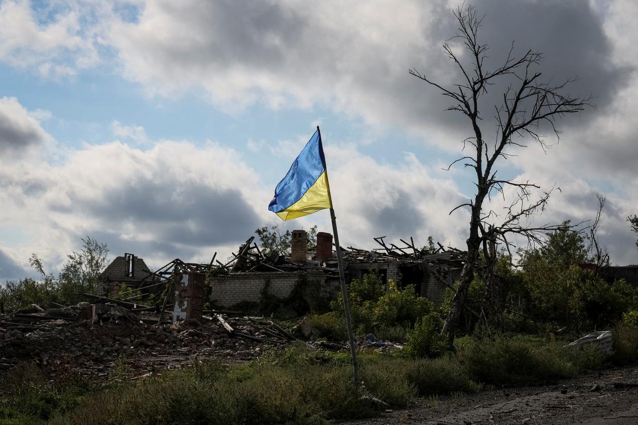 Ukrainian national flag is seen near destroyed buildings in the village of Dolyna