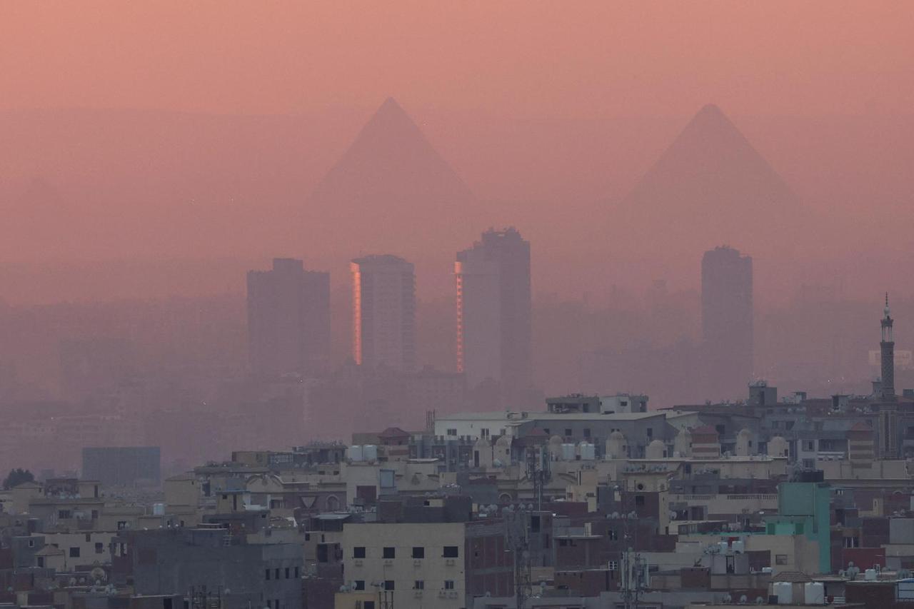 A view of old houses with hotels and the Great Pyramids during sunset with fog from air pollution over the Egypt's capital of Cairo