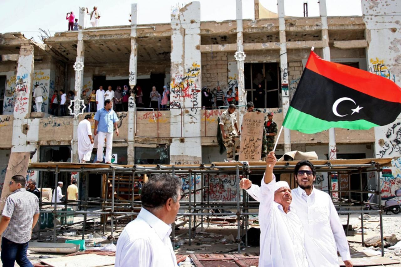 \'A Libyan elderly man waves the rebellion\'s flag as residents of Tripoli tour the destroyed Bab al-Aziziyah former headquarters of Libyan leader Moamer Kadhafi on September 1, 2011, as rebel forces 