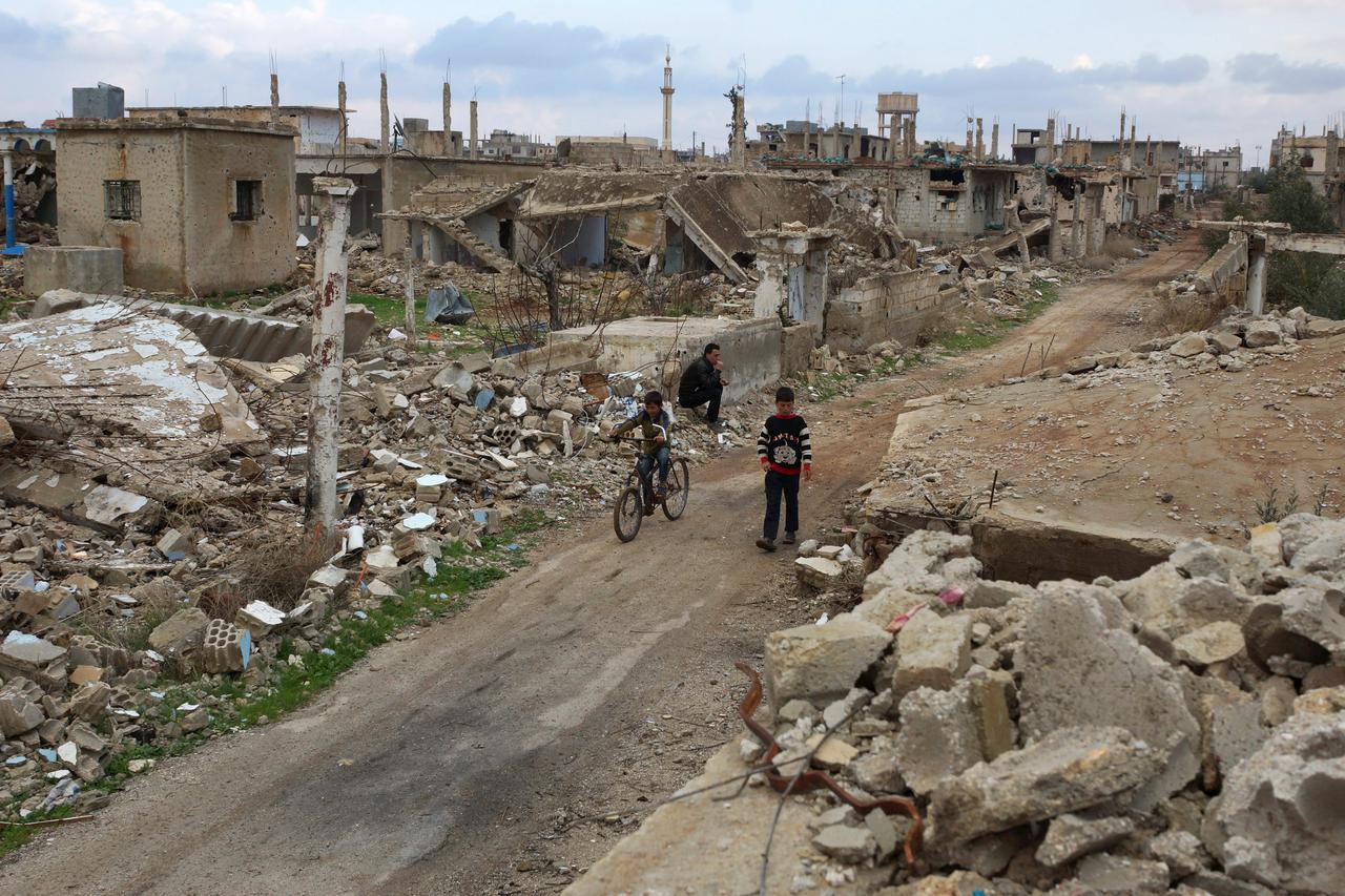 A boy rides a bicycle past a man sitting on rubble of a damaged house in the rebel held historic southern town of Bosra al-Sham, Deraa, Syria February 23, 2016. REUTERS/Alaa Al-Faqir      TPX IMAGES OF THE DAY     