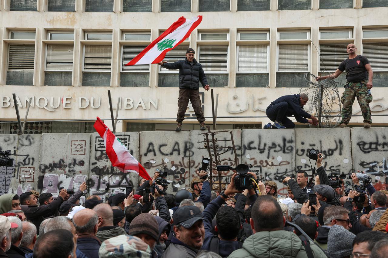 A demonstrator holds the Lebanese flag as he stands on a barricade during a protest over the deteriorating economic situation in front of the Central Bank building in Beirut, Lebanon March 30, 2023.