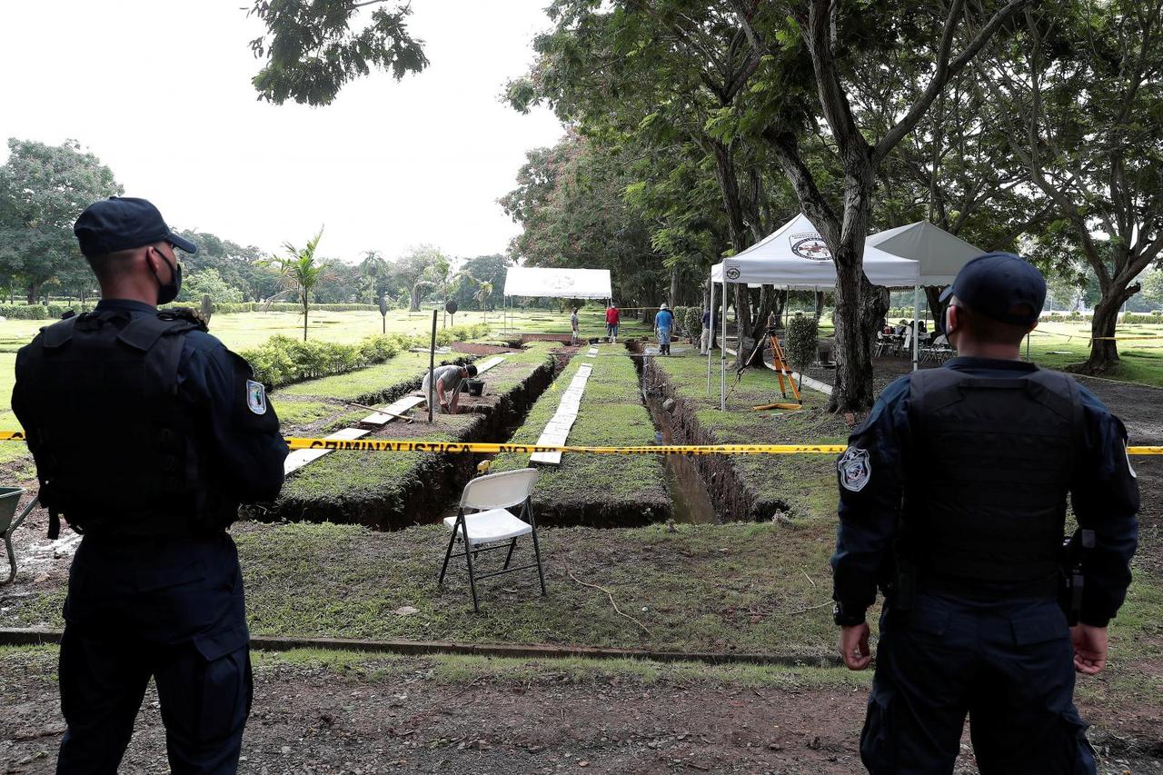Police officers keep watch as employees work to exhume bodies at a private cemetery as part of a search for victims of the 1989 invasion by the U.S. military action to topple strongman Manuel Noriega, in Panama City