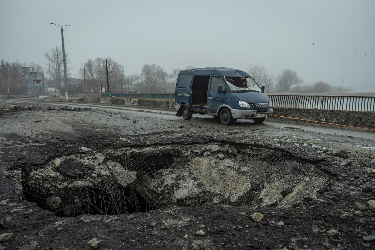 A local resident drives a damaged van past a bomb hole on a bridge in the town of Makariv