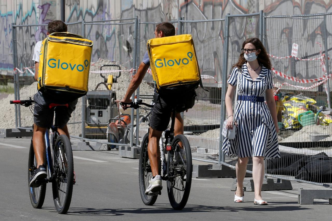 FILE PHOTO: A woman walks past Glovo food delivery couriers in Kyiv