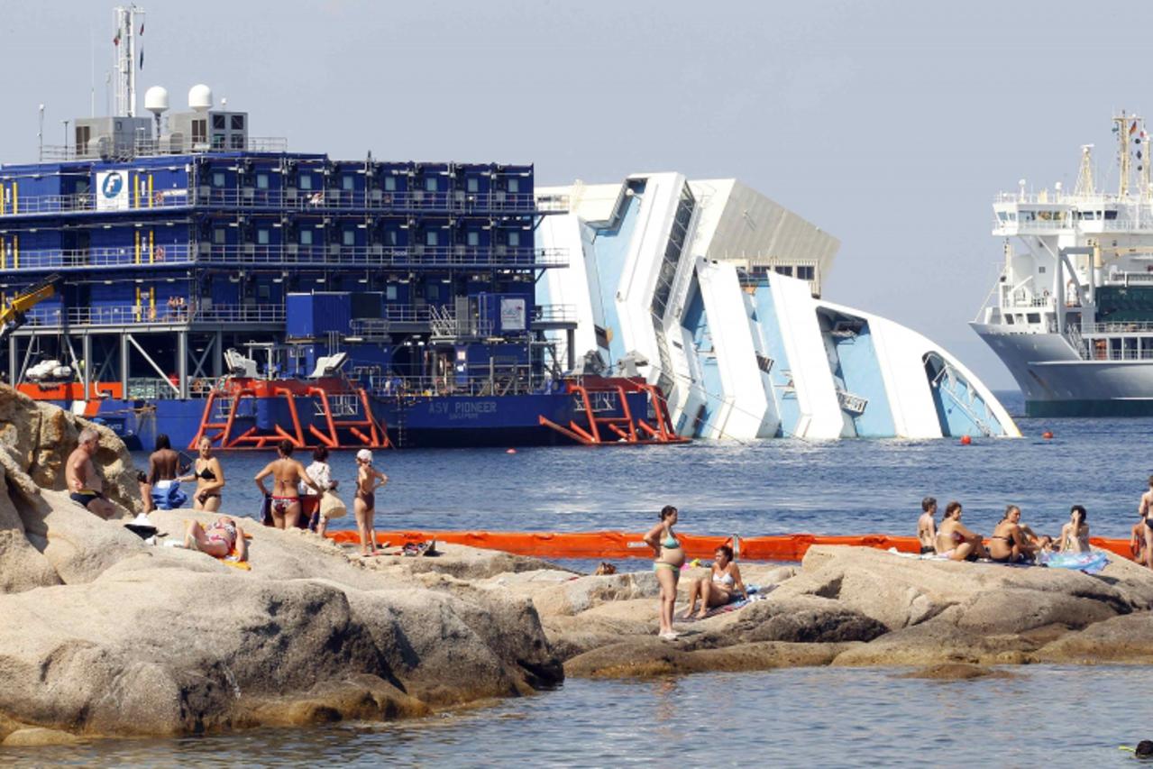 'People sunbathe in front of the capsized cruise liner Costa Concordia lying surrounded by cranes outside Giglio harbour July 17, 2013. The trial of the captain of the Costa Concordia cruise ship, whi