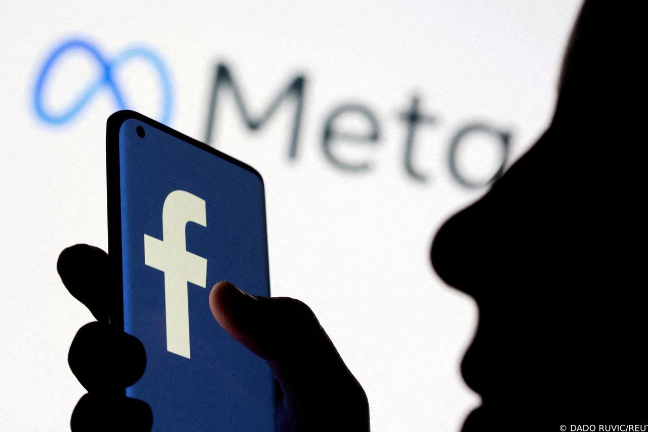 FILE PHOTO: Woman holds smartphone with Facebook logo in front of a displayed Facebook's new rebrand logo Meta in this illustration picture