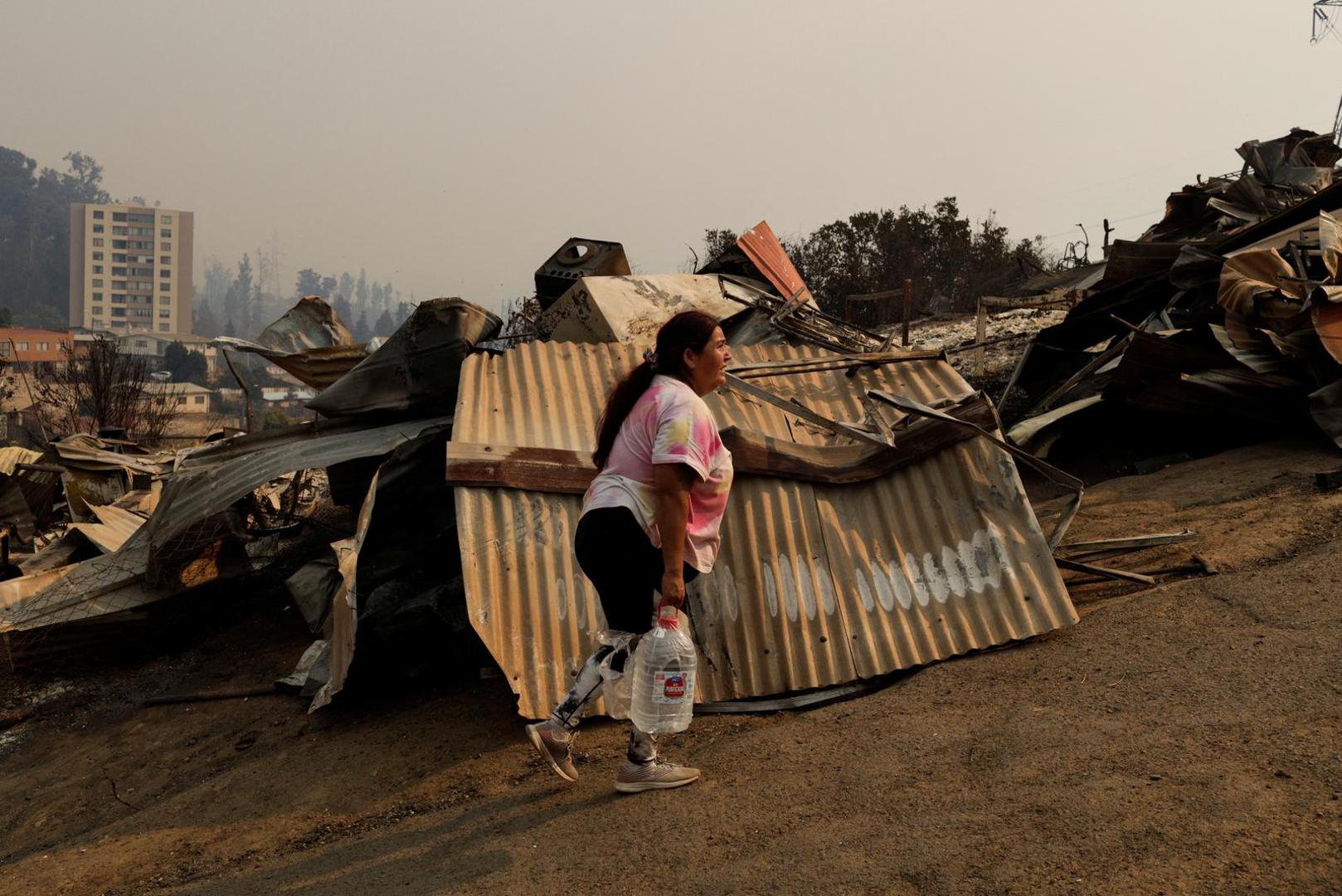 A woman walks past the remains of burnt houses following the spread of wildfires in Vina del Mar, Chile February 3, 2024. REUTERS/Sofia Yanjari Photo: SOFIA YANJARI/REUTERS