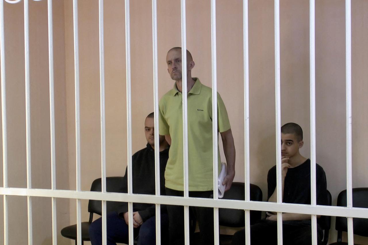 A still image shows Britons Aiden Aslin, Shaun Pinner and Moroccan Brahim Saadoun in a courtroom cage at a location given as Donetsk
