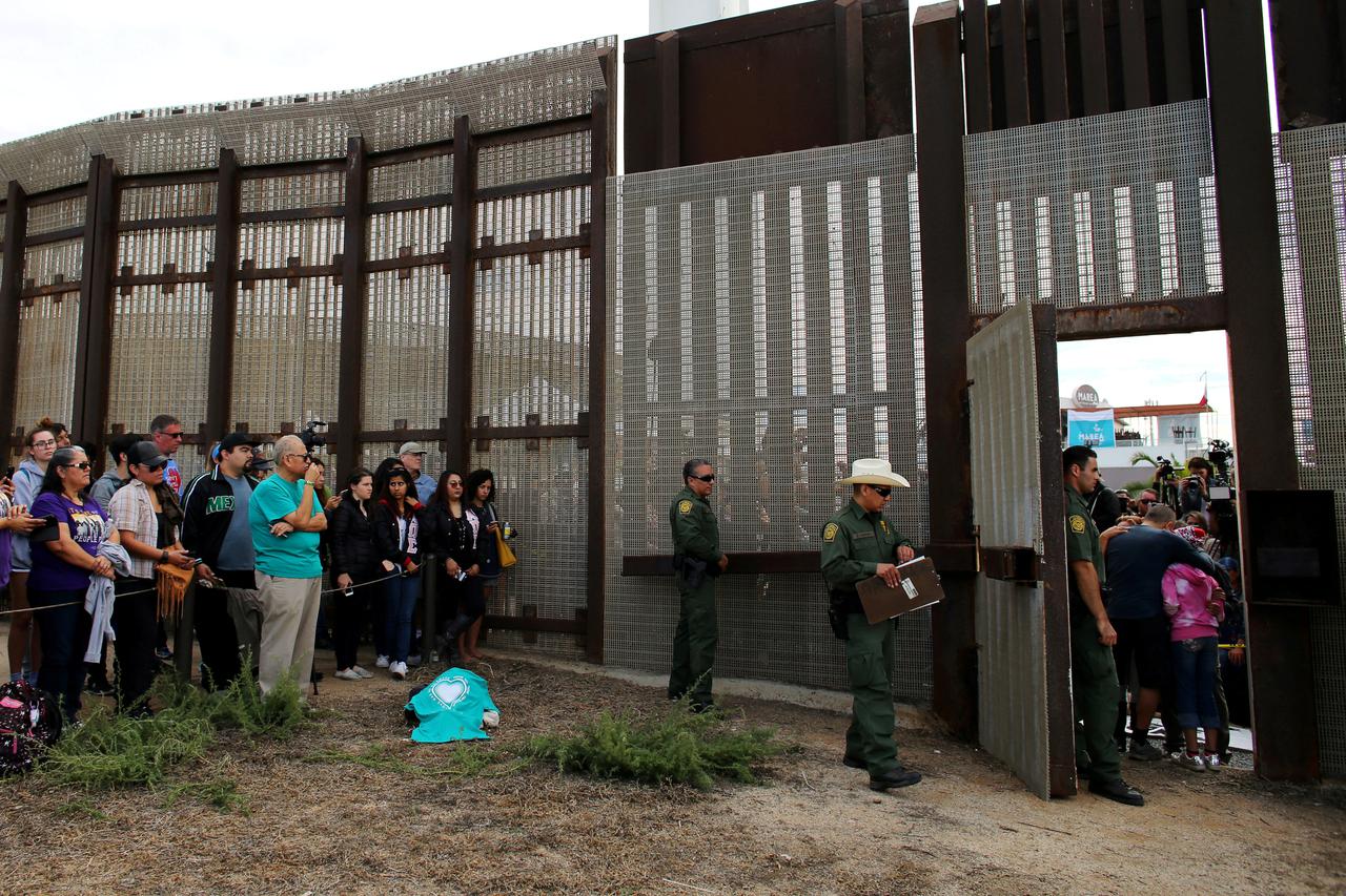 FILE PHOTO: U.S. Border patrol agents stand at an open gate on the fence along the Mexico border to allow Adrian Gonzalez-Morales and his daughter Aileen hug his parents Juan and Martha, as part of Universal Children's Day at the Border Field State Park, 