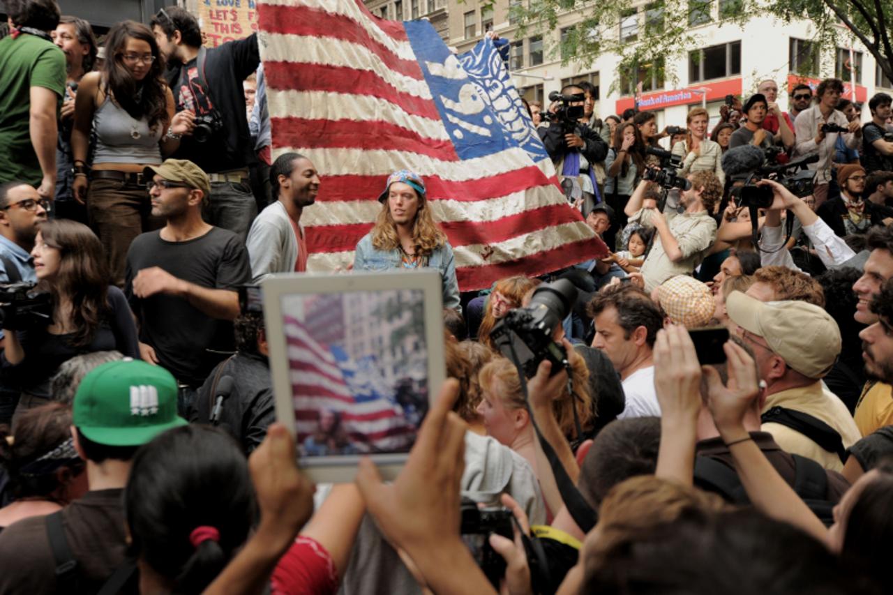 'A person with an iPad takes a photograph of a large flag as demonstrators with \'Occupy Wall Street\' occupy Zuccotti Park on September 30, 2011 in New York. The demonstrators are protesting bank bai