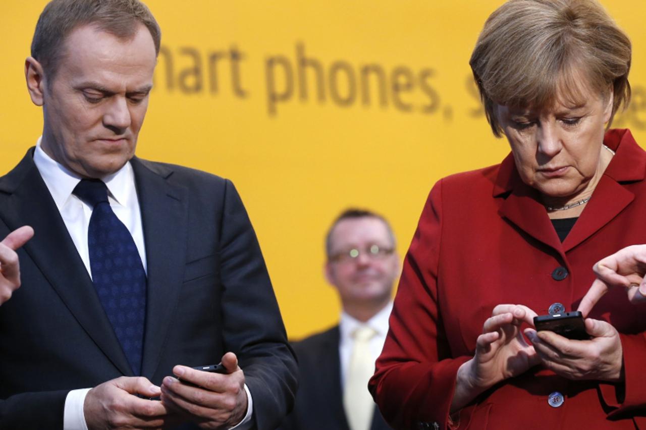 'German Chancellor Angela Merkel (R) and Poland's Prime Minister Donald Tusk use BlackBerry Z10 smartphones featuring high security Secusite software, used for governmental communication, at the boot