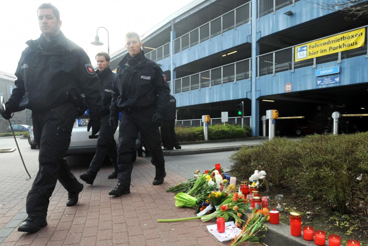 'Policemen walk past candles and flowers laid down on March 26, 2012 in front of a parking deck in Emden, western Germany, where an eleven-year old girl was found dead. Police said that they were sear