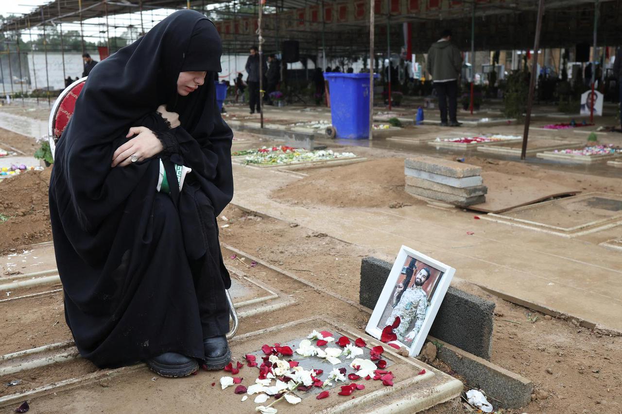 A woman reacts as she sits beside her husband's grave at Behesht-e Zahra cemetery, in Tehran