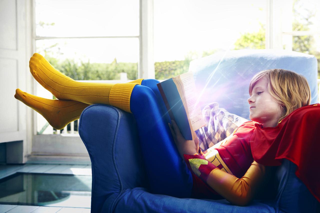 Little boy dressed as a super hero reading a book