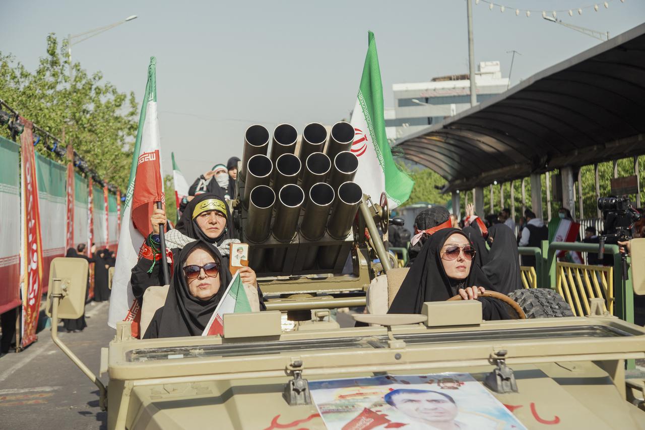 Women ride in a military-style vehicle carrying mounted weapons during a pro-government parade in Tehran, Iran