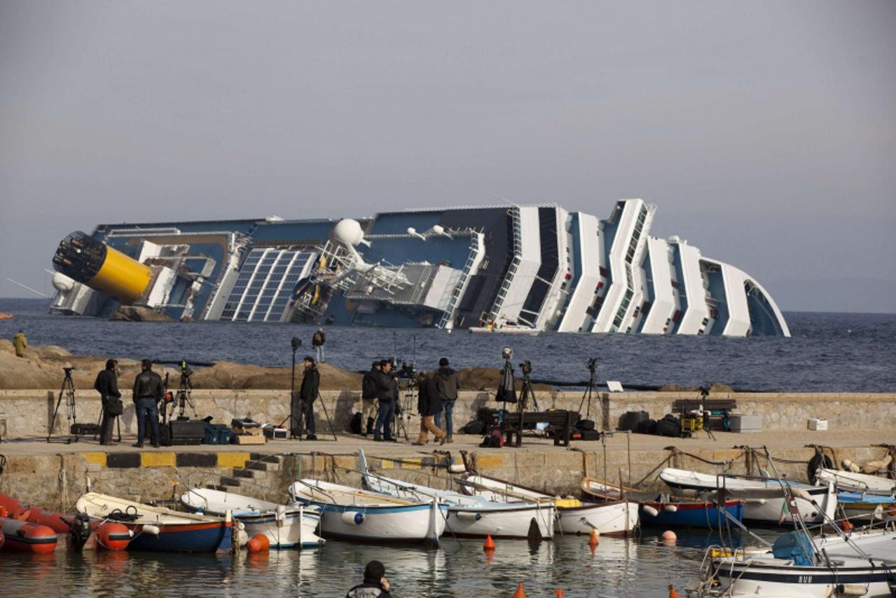 'TV crew stand on the dock in front of the Costa Concordia cruise ship after it ran aground off the west coast of Italy at Giglio island January 19, 2012. No deadline has been set for ending the searc