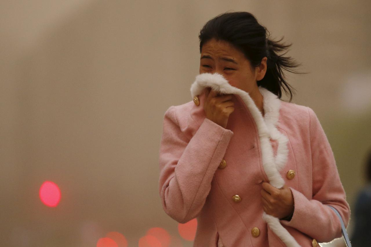 A woman covers her face with her jacket during a sand storm in Beijing April 15,  2015. A heavy sand storm is reported to have swept through 11 provinces in northern China on Wednesday. Beijing Meteorological Bureau has issued a yellow alert for the storm