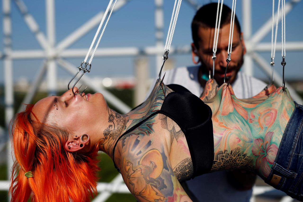 Professional body artist Dino Helvida (R), 27, inspects Kaitlin, 28, from the United States, as she is suspended from hooks pierced through her skin in Zagreb, Croatia June 7, 2016. REUTERS/Antonio Bronic      SEARCH 