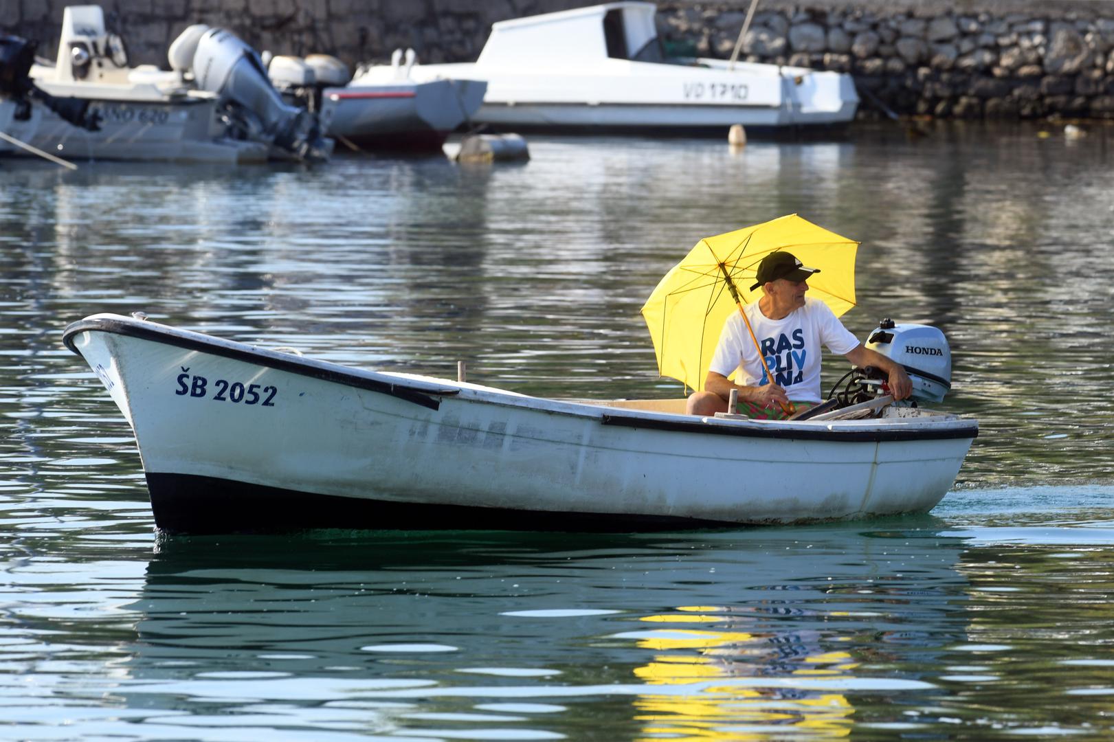 23.07.2022., Raslina - Spas od paklenih vrucina i jakoga sunca ovaj je mjestanin Rasline rijesio sa zutim kisobranom.  Photo: Hrvoje Jelavic/PIXSELL