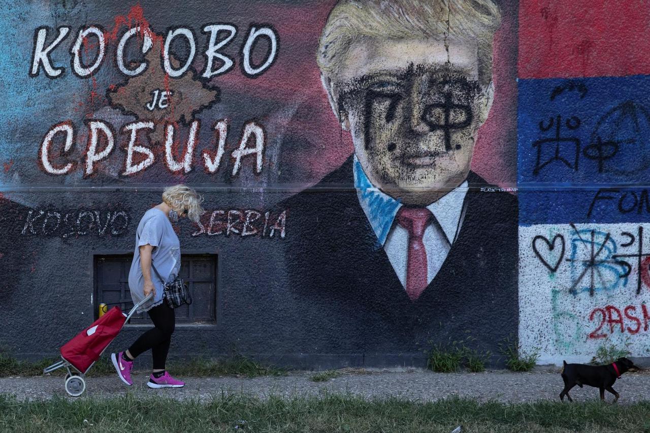 Woman walks with a dog in front of a mural depicting U.S. President Trump in Belgrade