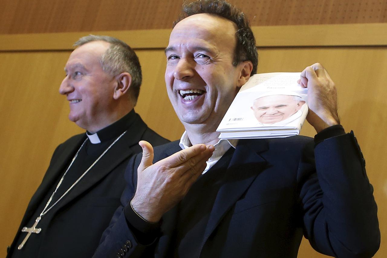 Italian actor Roberto Benigni (R) smiles as he holds a copy of Pope Francis' book 