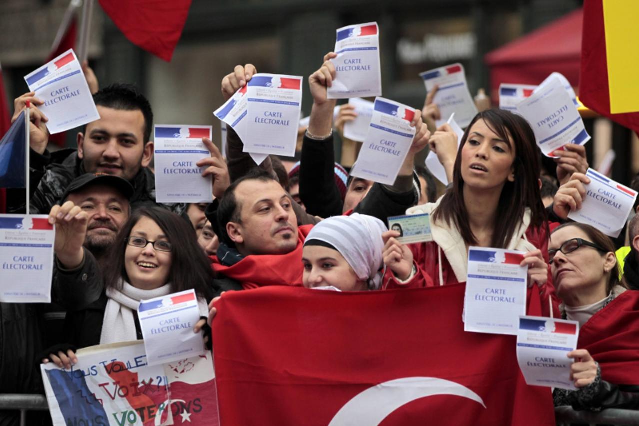 'Franco-Turks protesters hold French electoral cards and a Turkish flag as they attend a demonstration next to the National Assembly in Paris December 22, 2011 ahead of a parliamentary vote on a bill 