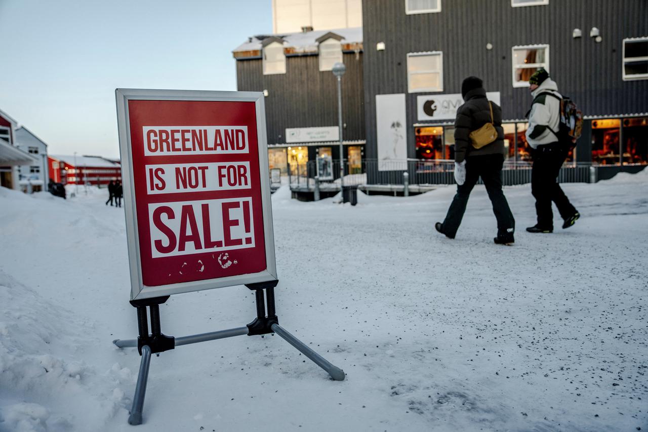 People walk past a sign placed on a street in Nuuk
