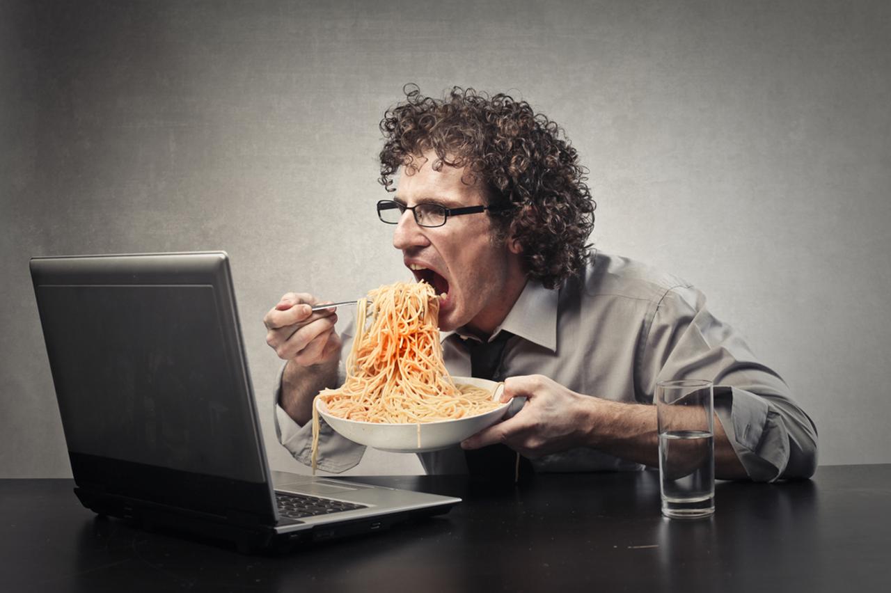 Čovjek jede ispred laptopa.Posao, ured, produktivnost