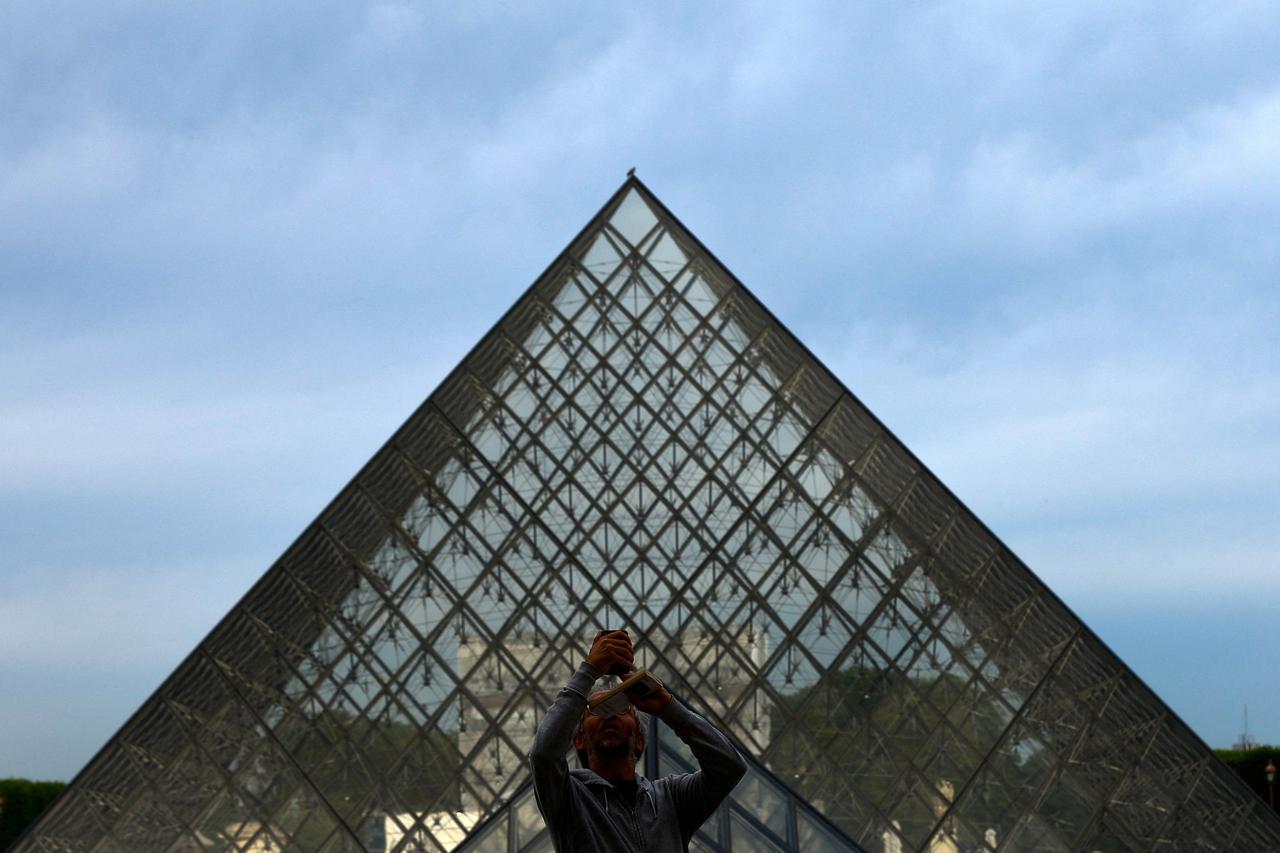 A man takes a selfie near the glass Pyramid of the Louvre museum in Paris