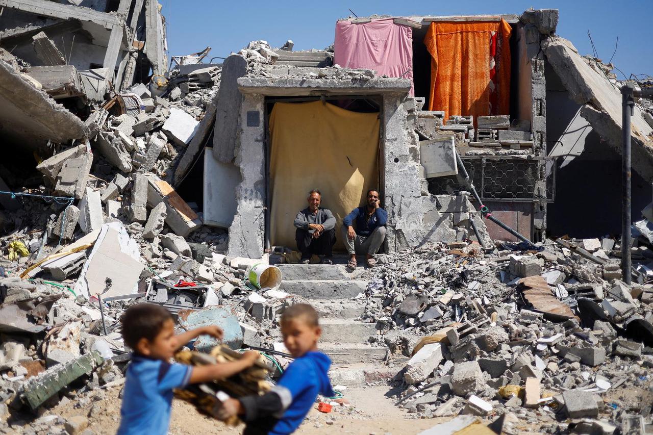 Palestinians sit at their house which was destroyed in an Israeli strike, amid the ongoing conflict between Israel and Hamas, in Khan Younis