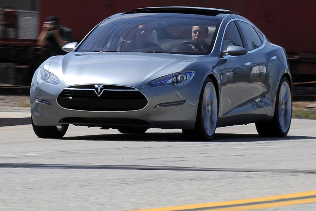 'Tesla Motors Chairman and CEO Elon Musk (in driver's seat) and chief designer Franz von Holzhausen (in passenger seat) drive the new Tesla Model S all-electric sedan out into the street as members o