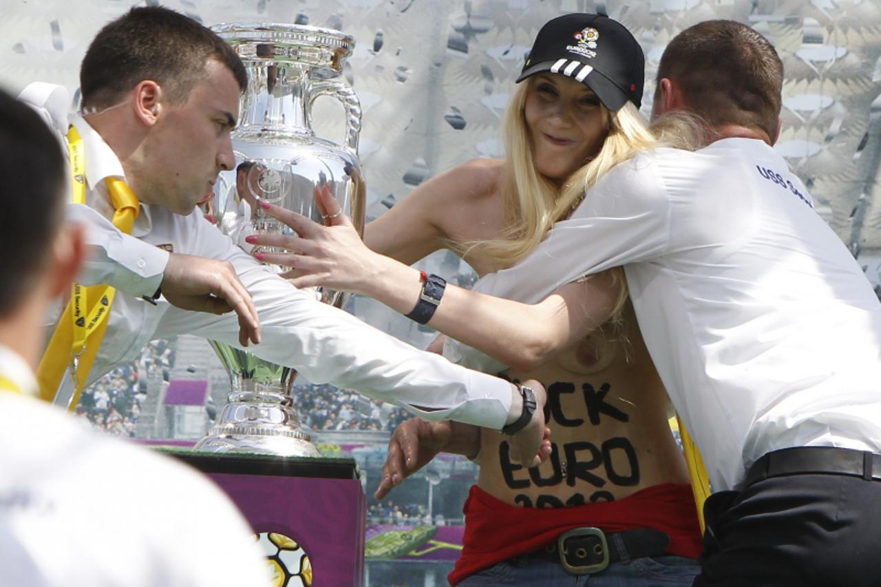 'Security guards detain a demonstrating activist from women\'s rights organisation Femen near the Euro 2012 trophy during its unveiling to the public in central Kiev May 12, 2012. The activist was pro