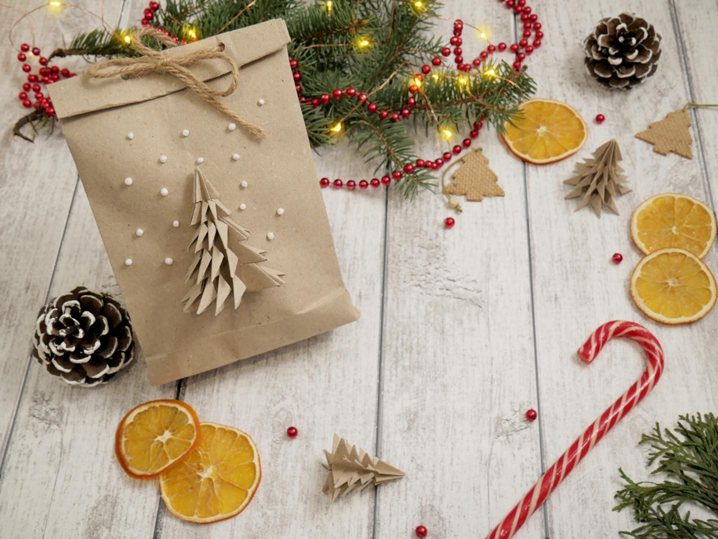 Preuređene papirnate vrećice: Ne bacajte papirnate vrećice iz trgovine, one se lako pretvore u blagdansku ambalažu. Okrenite ih, odrežite ručke ako treba i probušite dvije rupice za špagu. Na vrh dodajte pečat od kartona ili jednostavnu naljepnicu od recikliranog papira. Vrećicu možete i oslikati ili zalijepiti izrezane zvjezdice od starog papira.