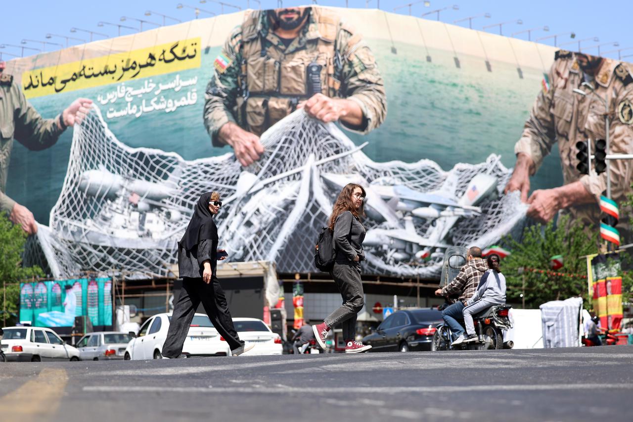 Iranians walk past a huge billboard carrying a sentence reading in Persian 'The Strait of Hormuz remains closed' at Enghelab Square in Tehran, Iran