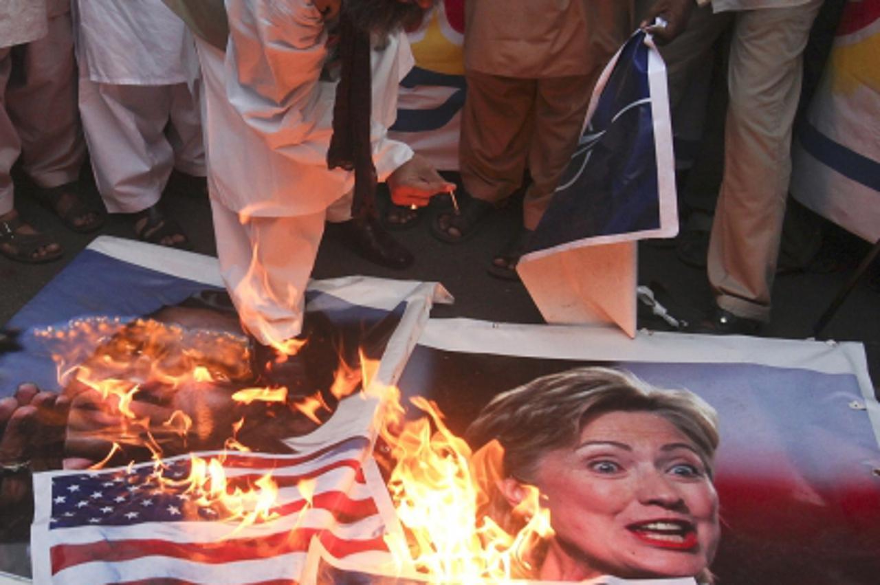 'A supporter of religious political party Sunni Tehreek sets ablaze the images of U.S. President Barack Obama (L), U.S. Secretary of State Hillary Clinton (R), the NATO and the U.S. flags during a dem