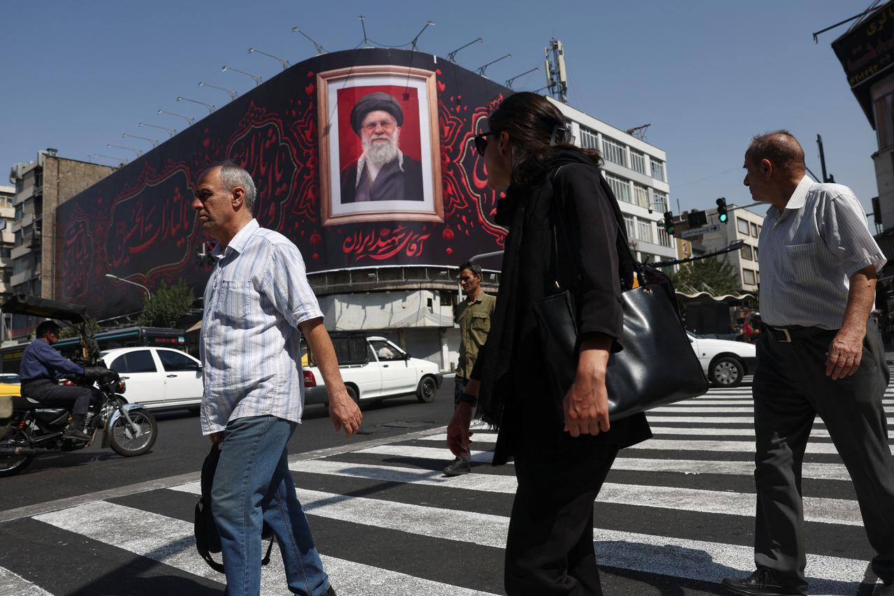 People walk past a billboard with an image of Iran's late Supreme Leader Ayatollah Ali Khamenei in Tehran, Iran