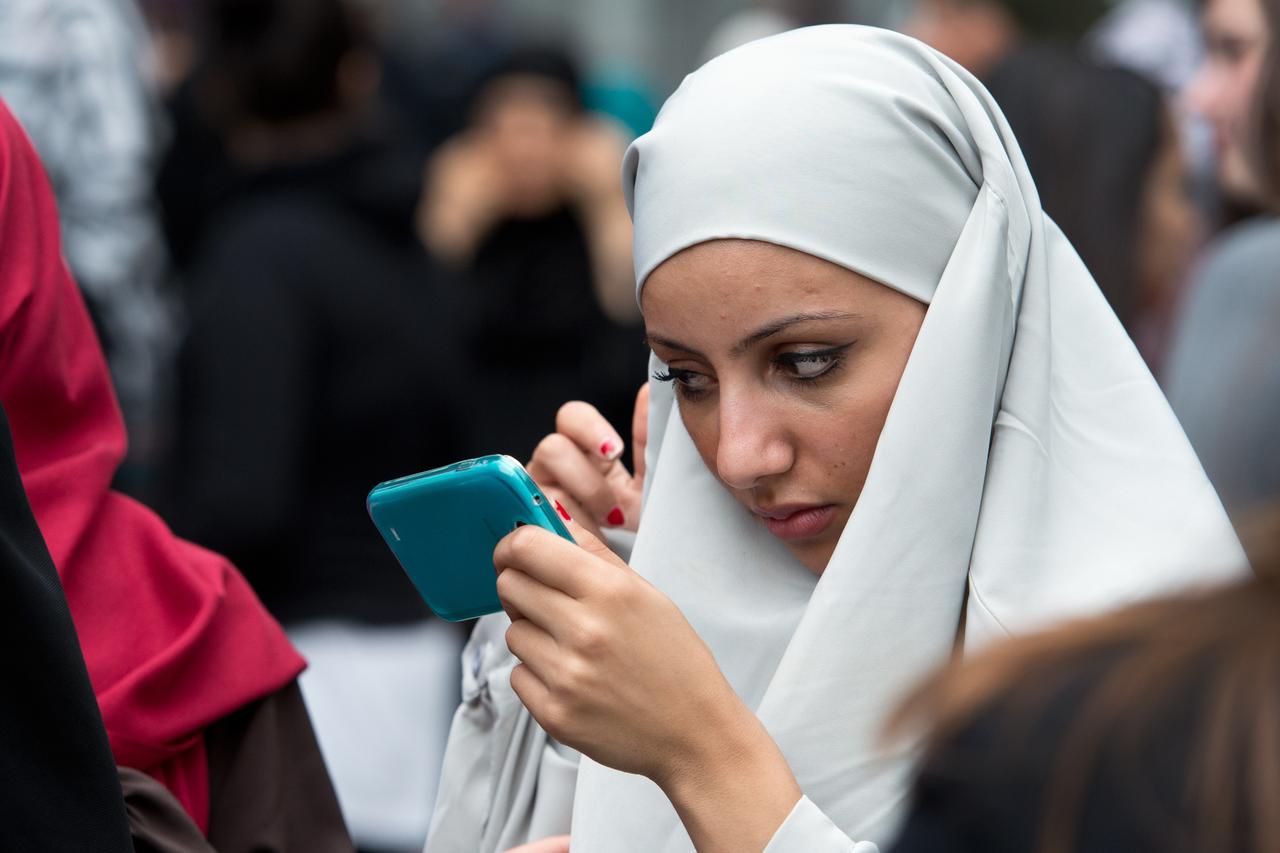 A woman uses her mobile as a mirror to adjust her head scarf during a rally of radical salafist preacher Pierre Vogel in Offenbach/Main, Germany, 28 Juen 2014. The police was in place to prevent a clash with counter-protestors. Photo: BORIS ROESSLER/dpa/D