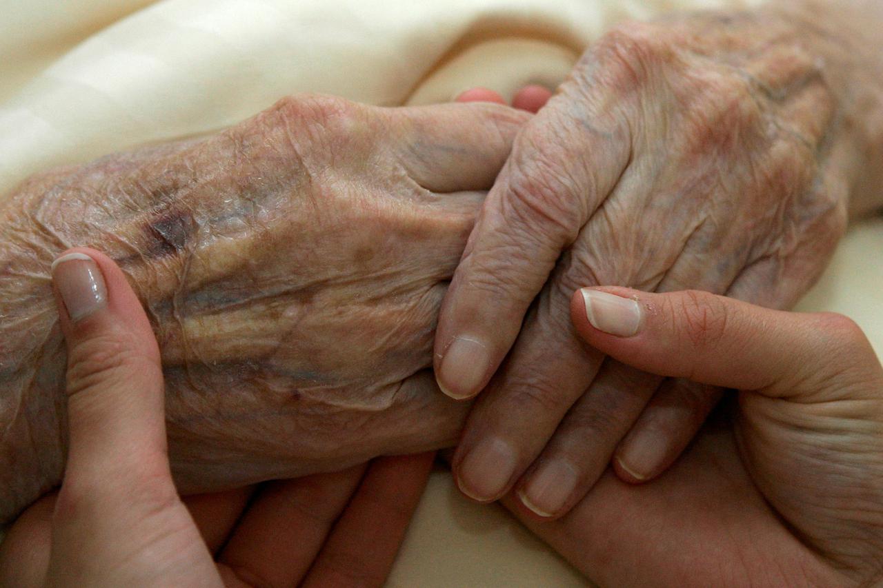 FILE PHOTO: A young carer holds the hands of an elderly woman in a residential home for the elderly in Planegg near Munich, Germany.